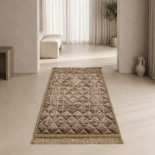 Mocha textured velvet prayer mat (janamaz) with embroidered geometric knot border and lantern, laid flat in a bright room